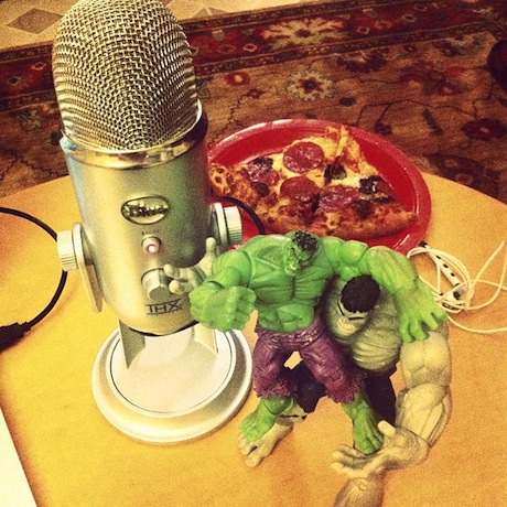 Still life photograph of a microphone, two Hulks fighting, and a slice of pizza.